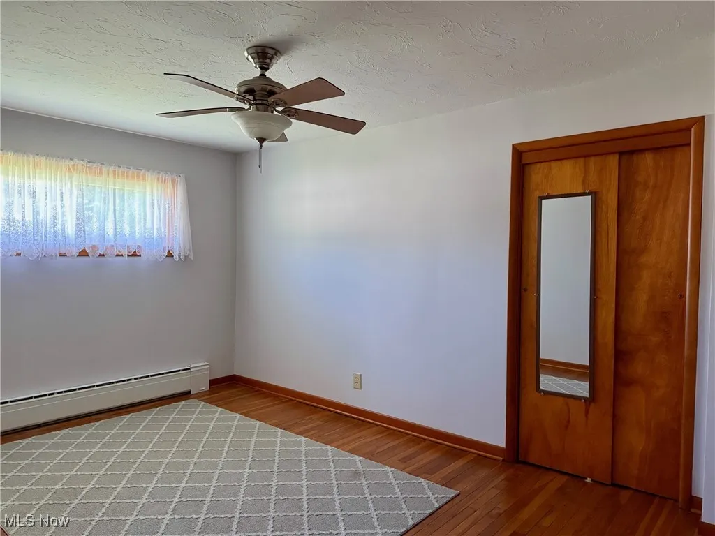 Unfurnished bed room featuring hardwood / wood-style floors, baseboard heating, a textured ceiling, and a ceiling fan