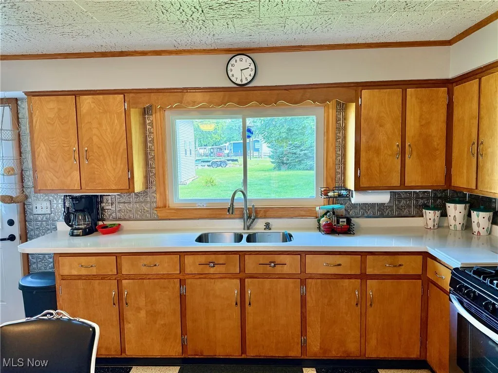 Kitchen with brown cabinets, light countertops, crown molding, tasteful backsplash, and range with gas stovetop