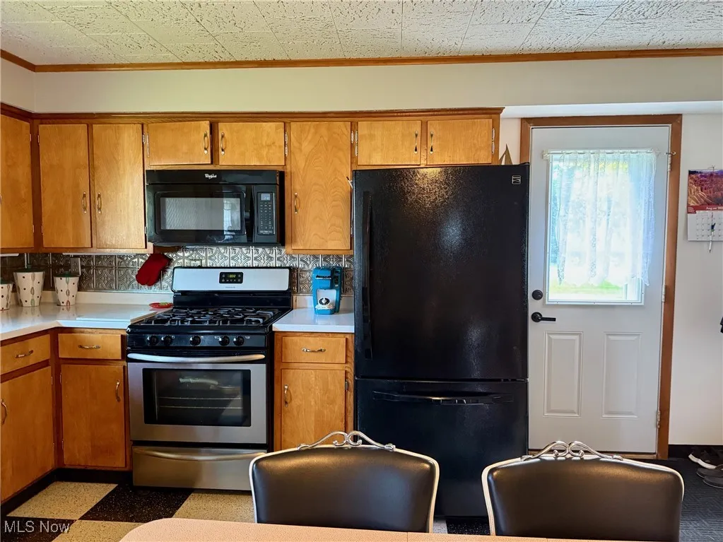 Kitchen with black appliances, brown cabinets, light countertops, and ornamental molding