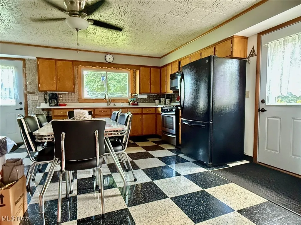 Kitchen with black appliances, dark flooring, brown cabinets, light countertops, and crown molding