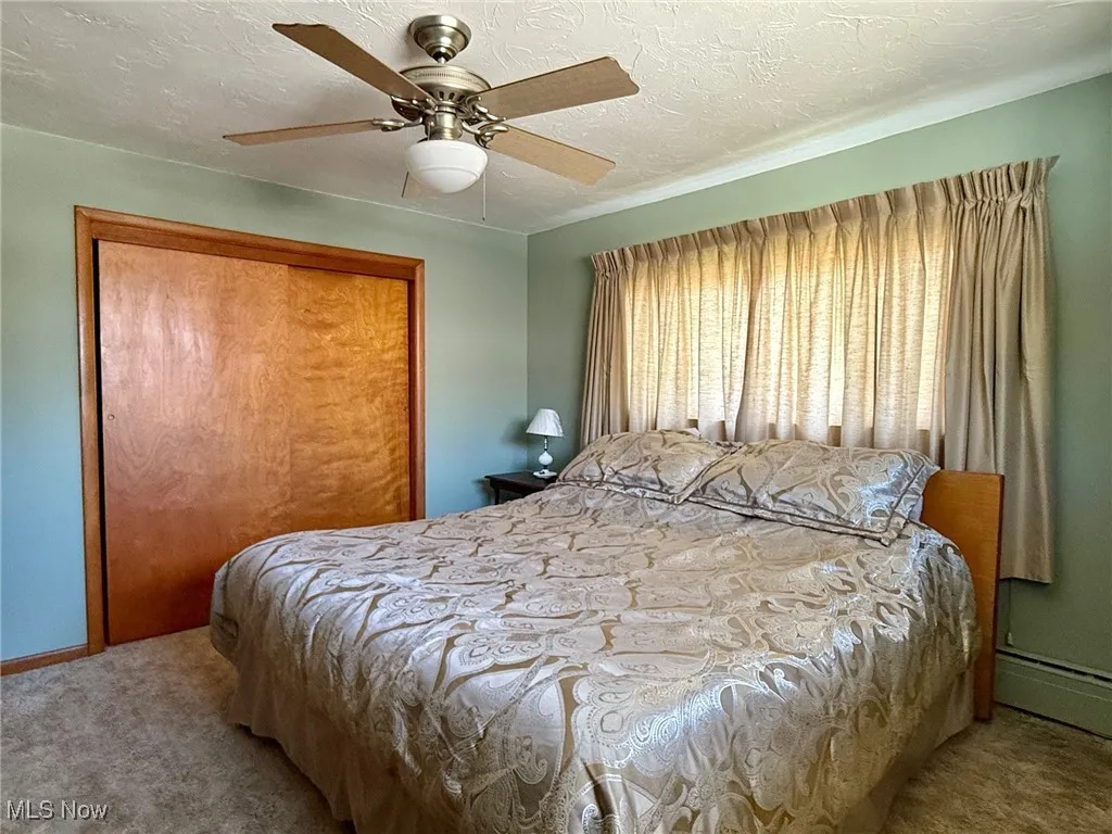 Bedroom featuring a textured ceiling, a closet, carpet, ceiling fan, and baseboard heating