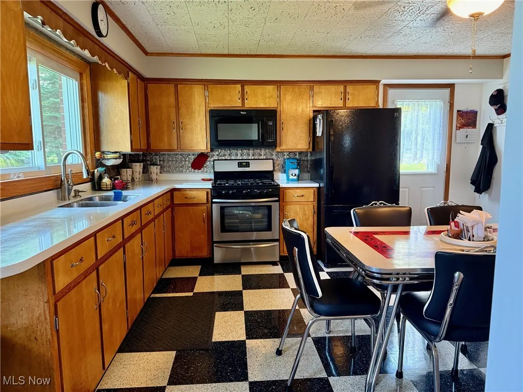 Kitchen featuring brown cabinetry, black appliances, light countertops, dark flooring, and ornamental molding