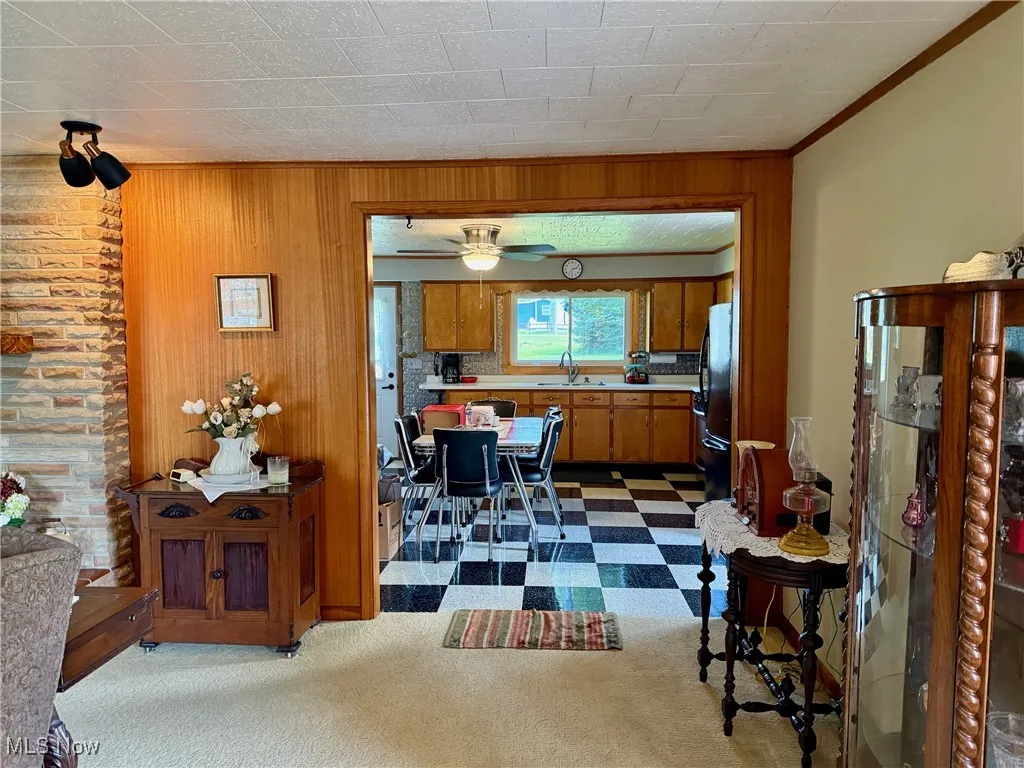 Dining space featuring wooden walls, dark colored carpet, crown molding, and a ceiling fan