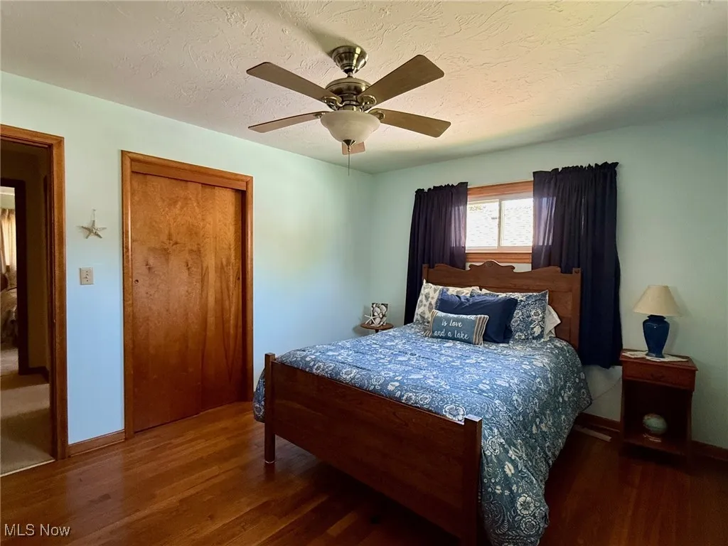 Bedroom with a textured ceiling, wood finished floors, a closet, and a ceiling fan