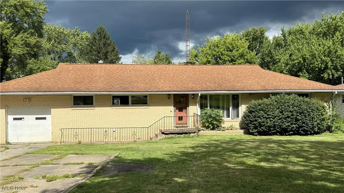 Single story home featuring a garage, brick siding, a front yard, driveway, and covered porch
