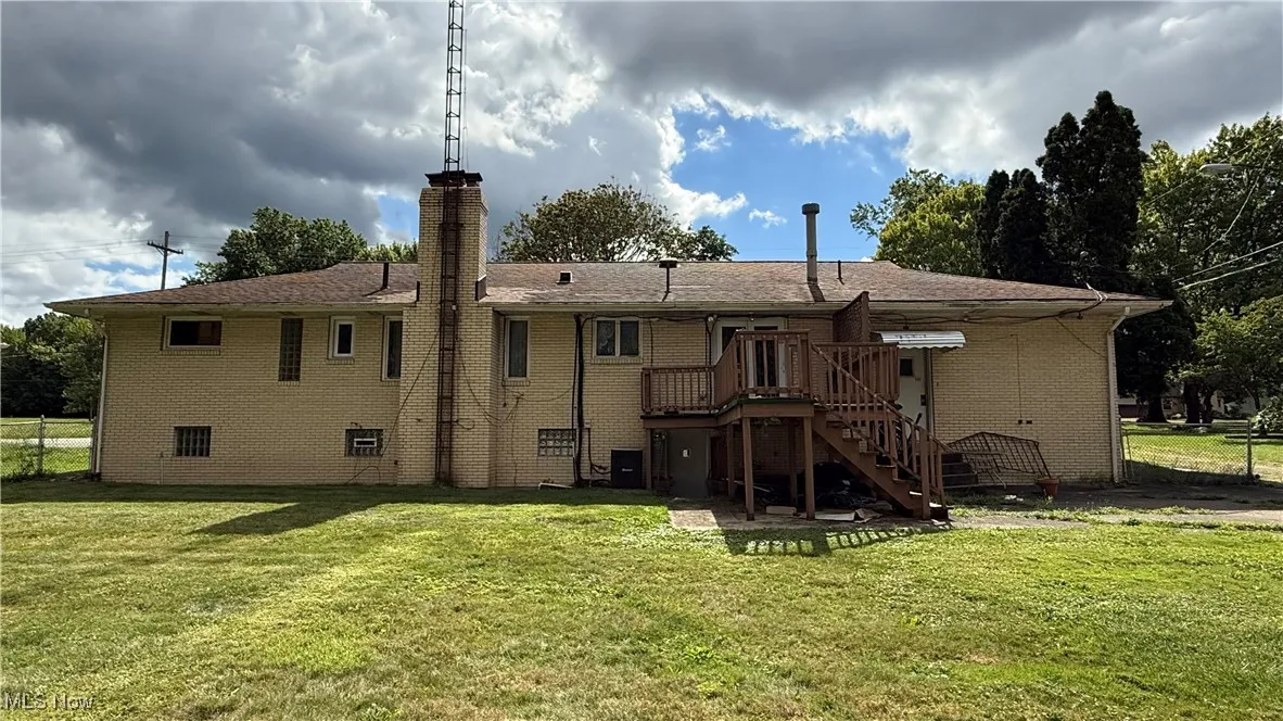 Back of property featuring brick siding, a lawn, a chimney, and a wooden deck