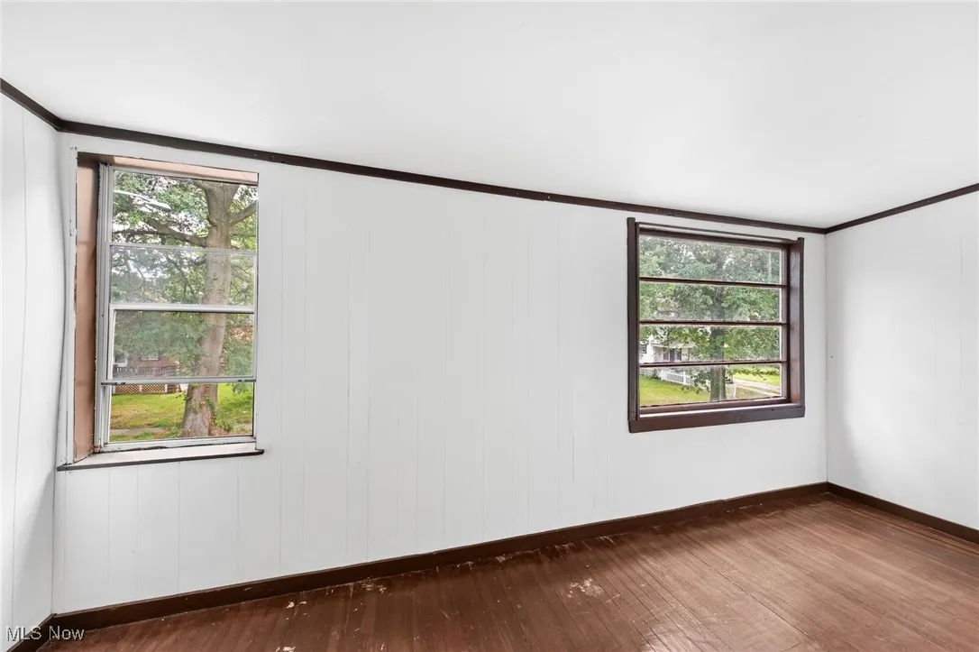 Empty room with crown molding, dark wood-style flooring, and wooden walls