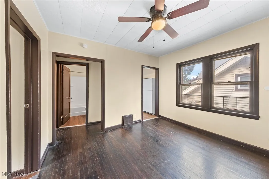 Unfurnished bedroom with dark wood-style floors, freestanding refrigerator, and ceiling fan