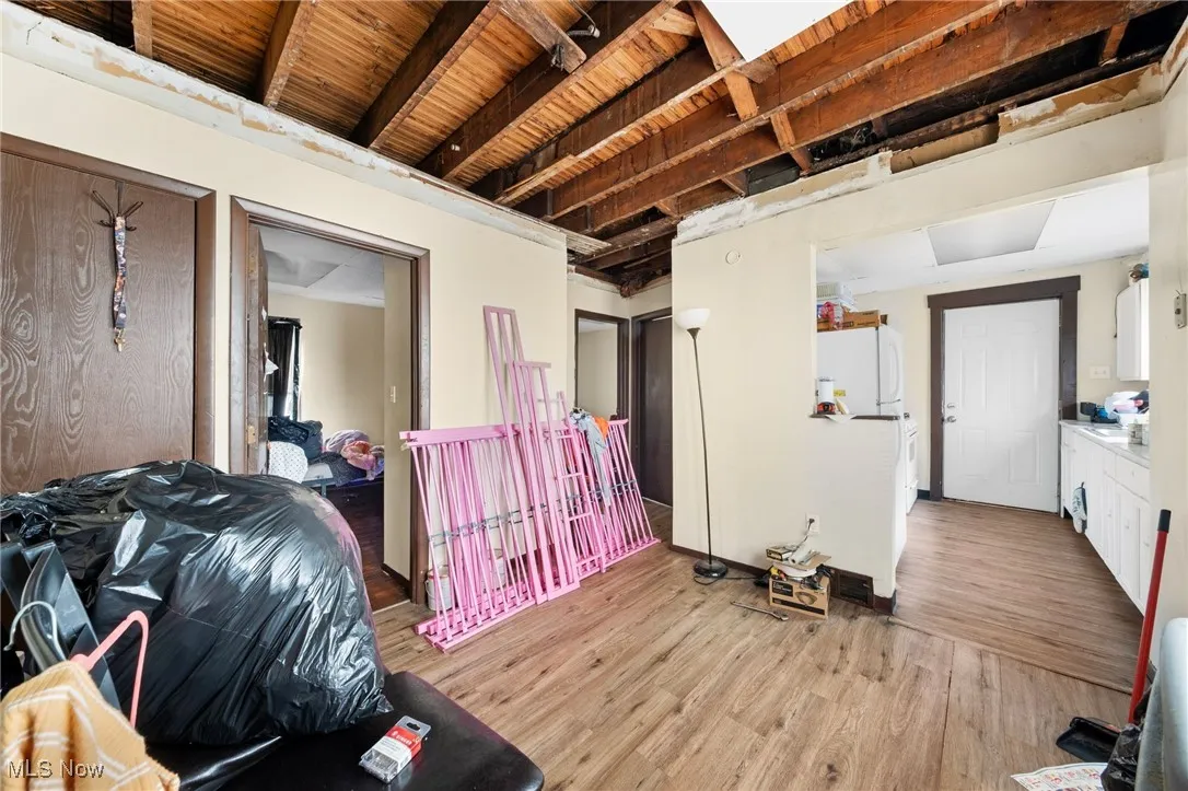 Bedroom featuring light wood-style floors, freestanding refrigerator, and beam ceiling