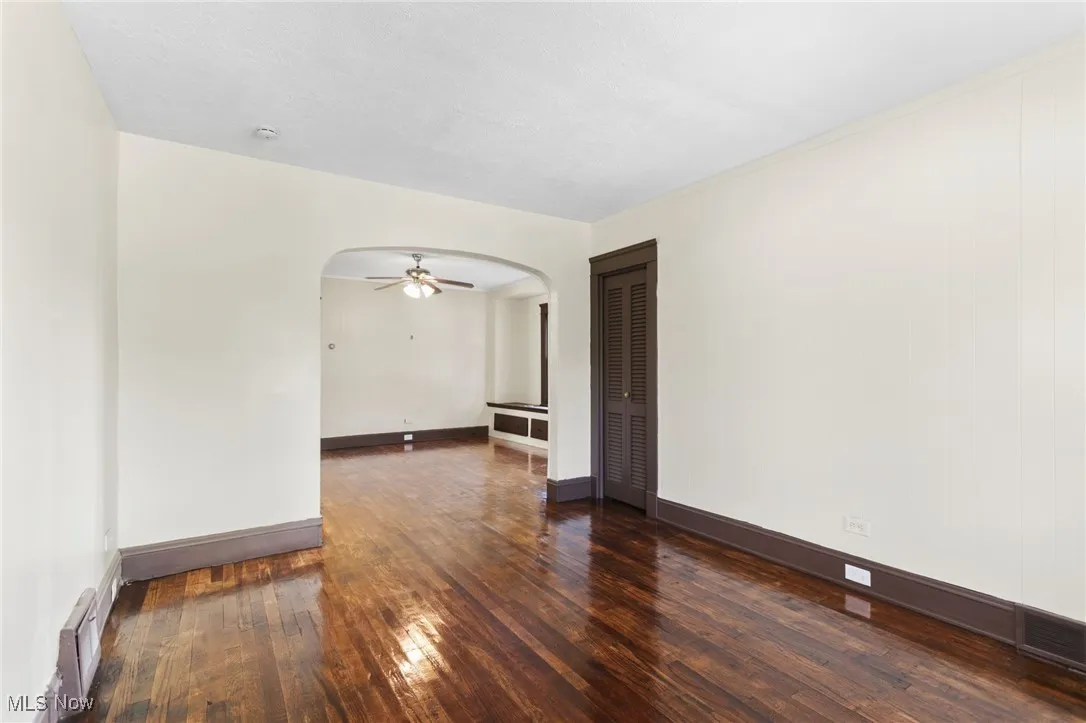Spare room featuring dark wood-style floors, arched walkways, and a ceiling fan