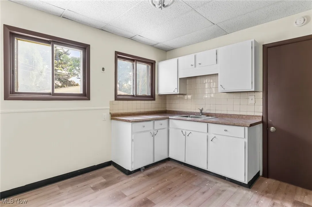Kitchen featuring white cabinets, tasteful backsplash, light wood finished floors, a drop ceiling, and dark countertops