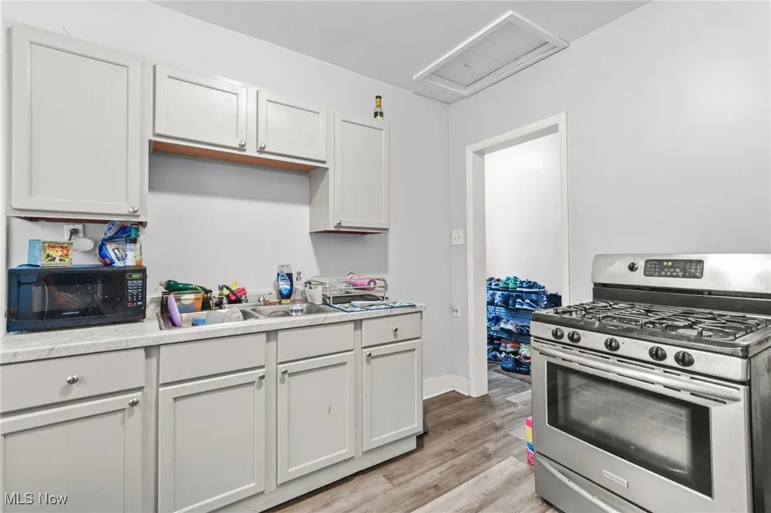 Kitchen with stainless steel gas stove, light countertops, light wood-type flooring, black microwave, and white cabinets
