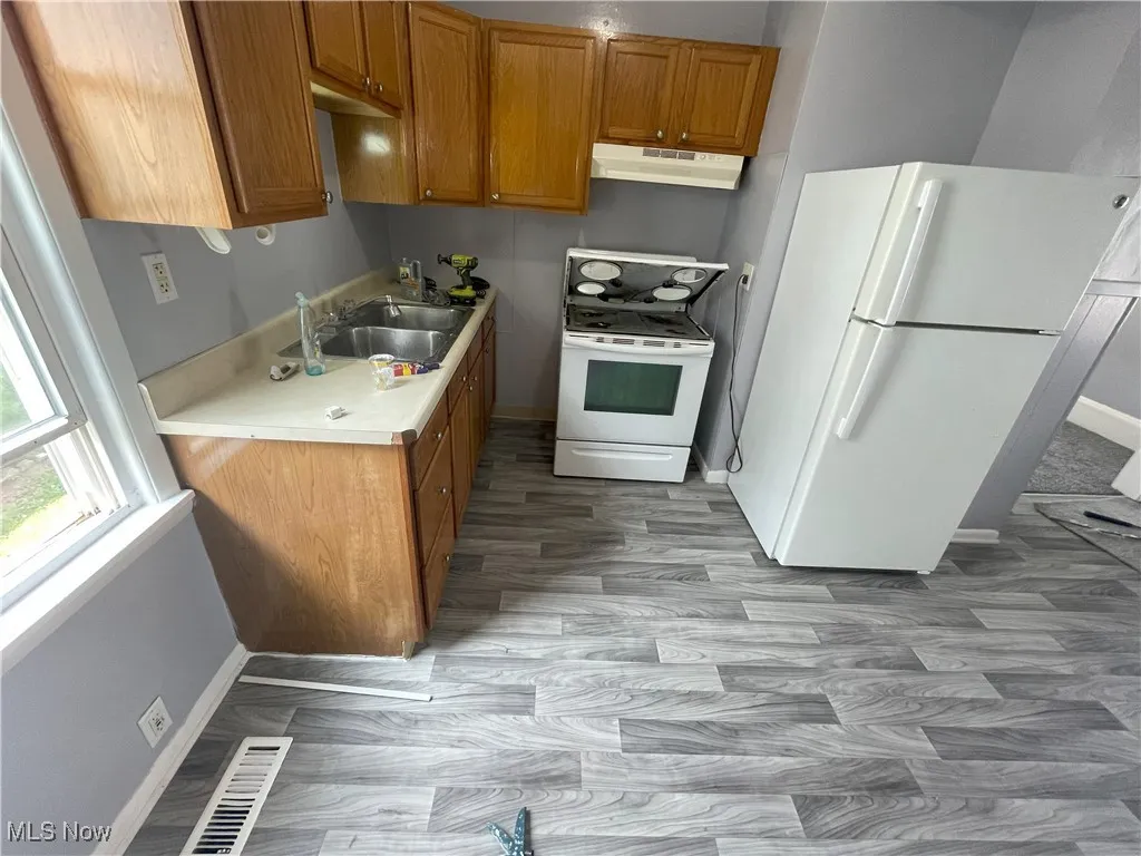 Kitchen featuring brown cabinetry, white appliances, light countertops, under cabinet range hood, and light wood-style floors