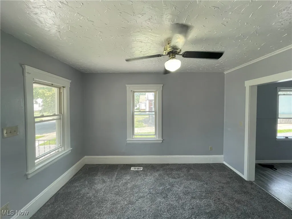 Empty room with healthy amount of natural light, dark carpet, a textured ceiling, and a ceiling fan