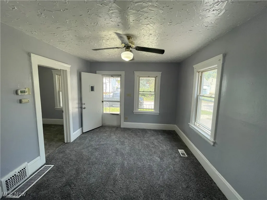 Empty room featuring dark colored carpet, a textured ceiling, and ceiling fan