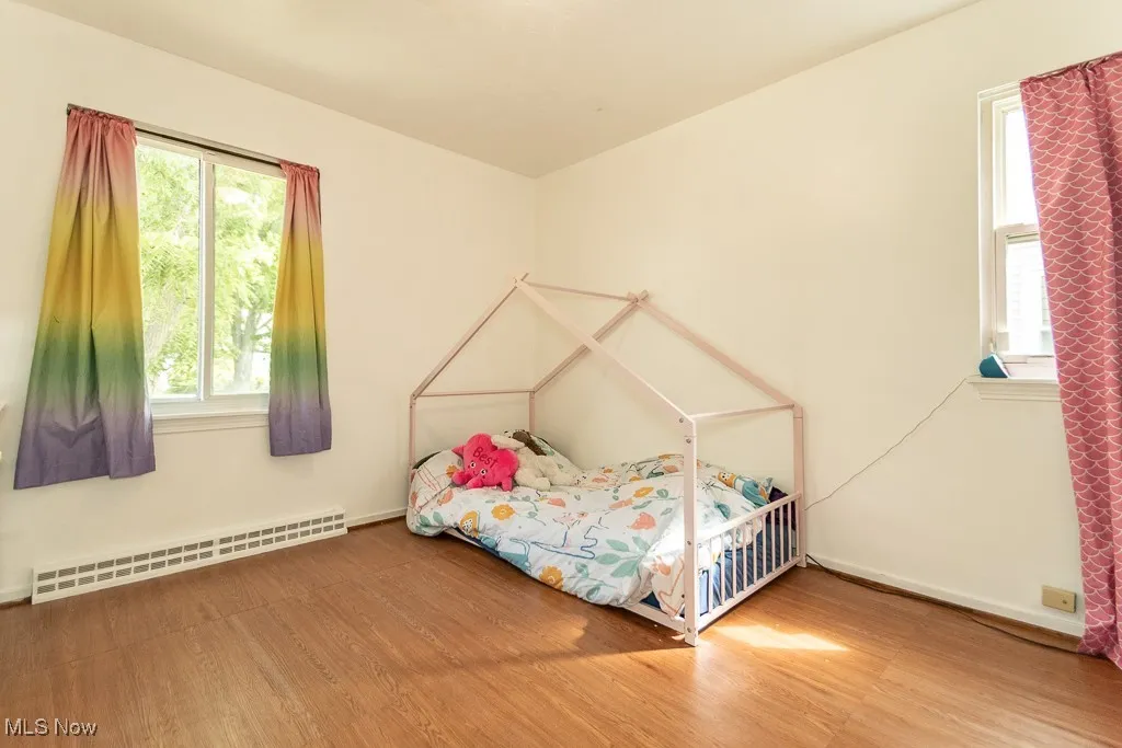 Bedroom with a baseboard heating unit, wood finished floors, and multiple windows