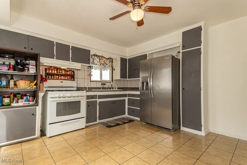Kitchen with white range with gas cooktop, stainless steel refrigerator with ice dispenser, dark countertops, light tile patterned floors, and tasteful backsplash