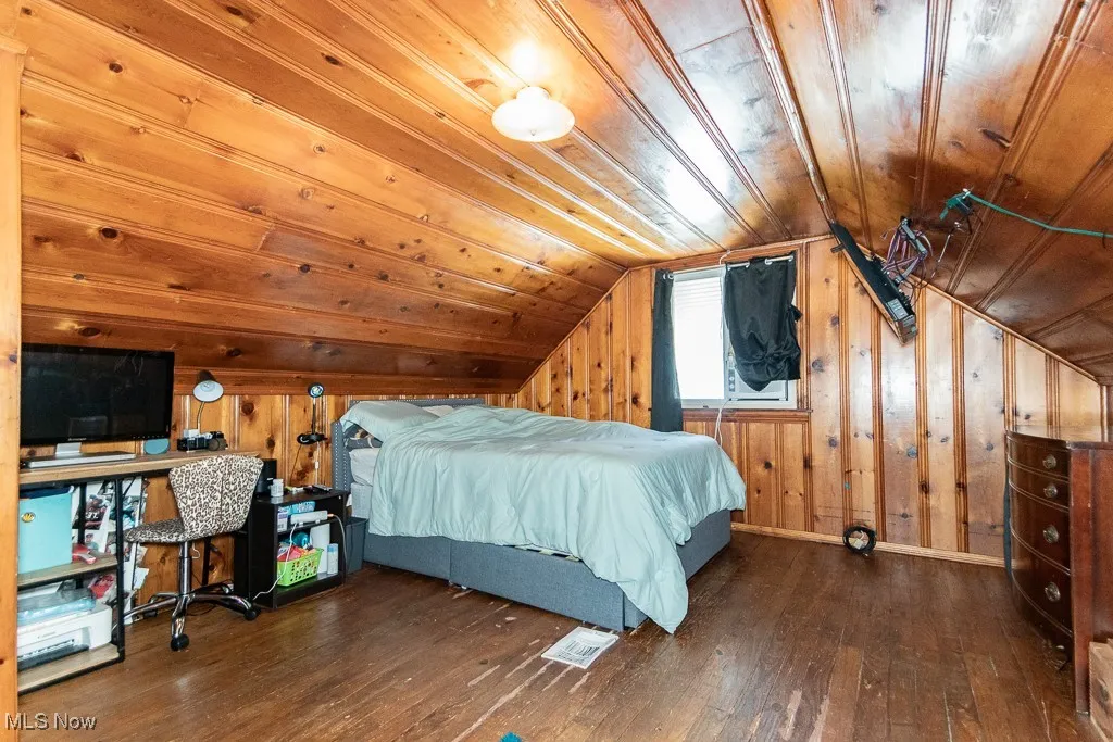 Bedroom with dark wood-type flooring, wooden walls, vaulted ceiling, and wood ceiling