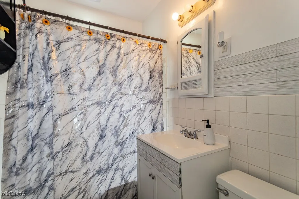 Full bathroom with vanity, tile walls, and a shower with shower curtain