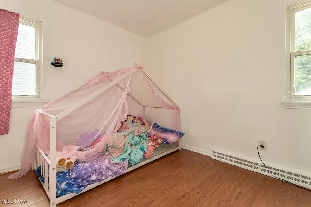 Bedroom featuring multiple windows, wood finished floors, and a baseboard heating unit