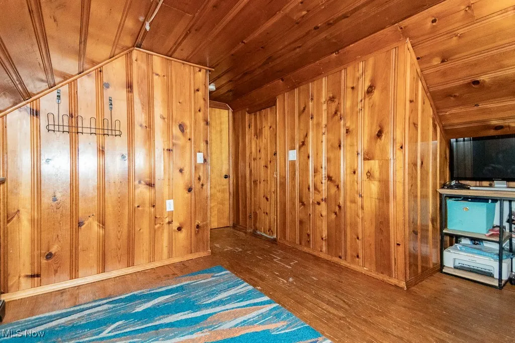 Empty room with dark wood-style flooring, wood ceiling, and wood walls