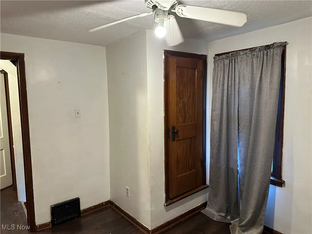 Unfurnished bedroom with a textured ceiling, dark wood-style flooring, and a ceiling fan