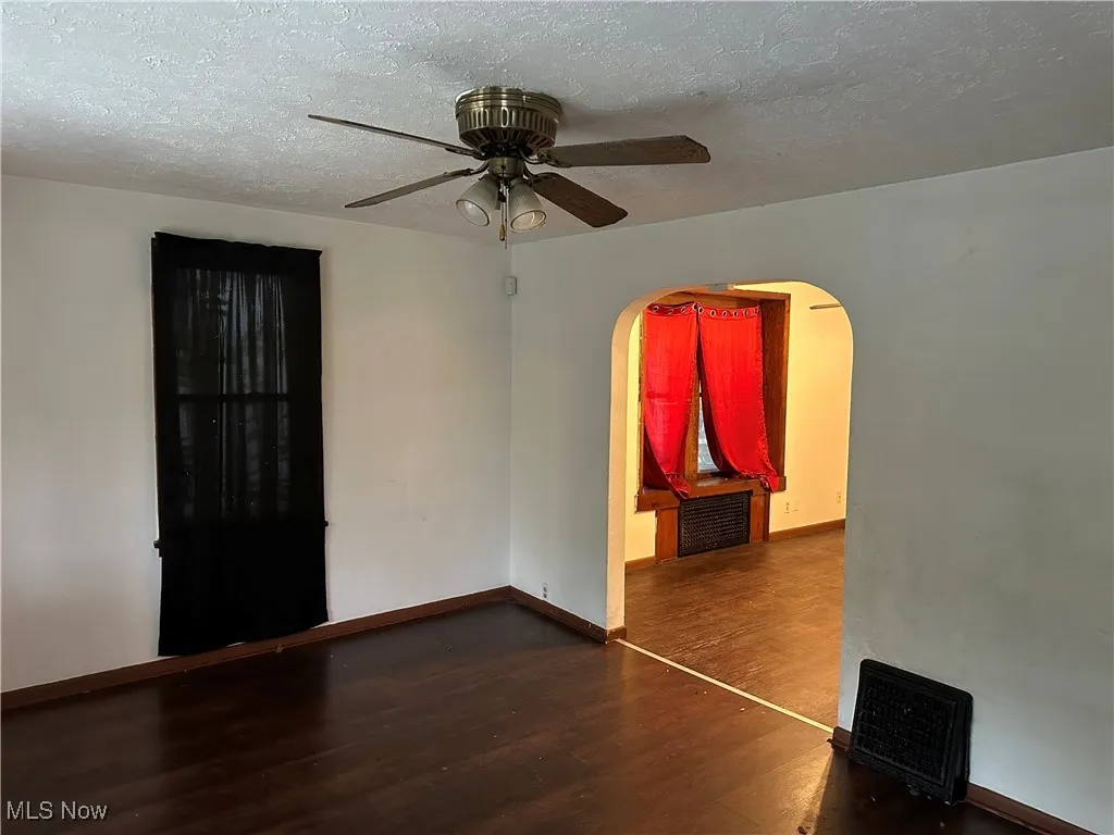 Empty room featuring a textured ceiling, dark wood finished floors, arched walkways, and ceiling fan