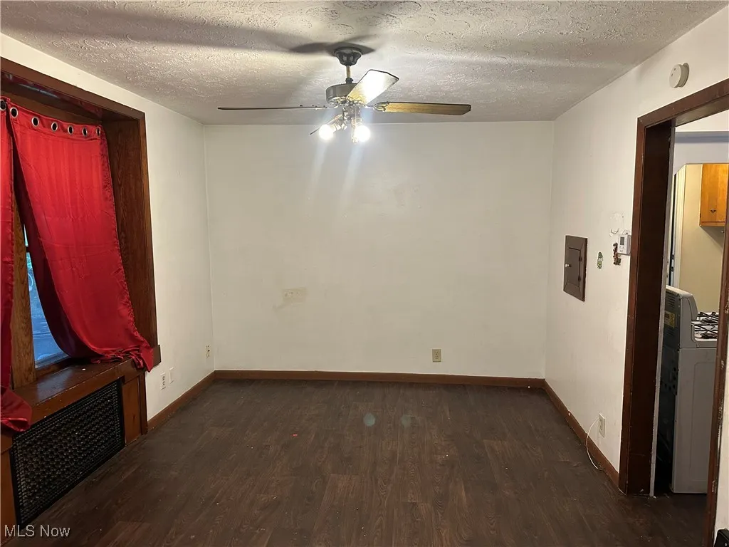 Unfurnished room with dark wood-style floors, a textured ceiling, radiator heating unit, ceiling fan, and electric panel