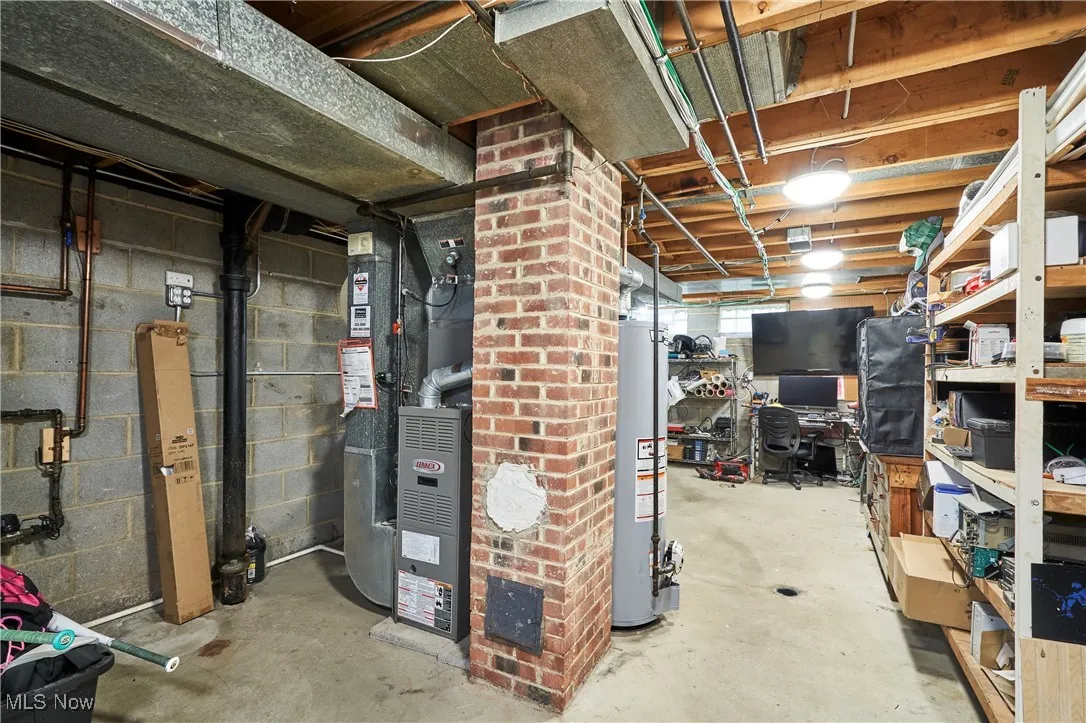 Unfinished below grade area with heating unit, gas water heater, and an office area