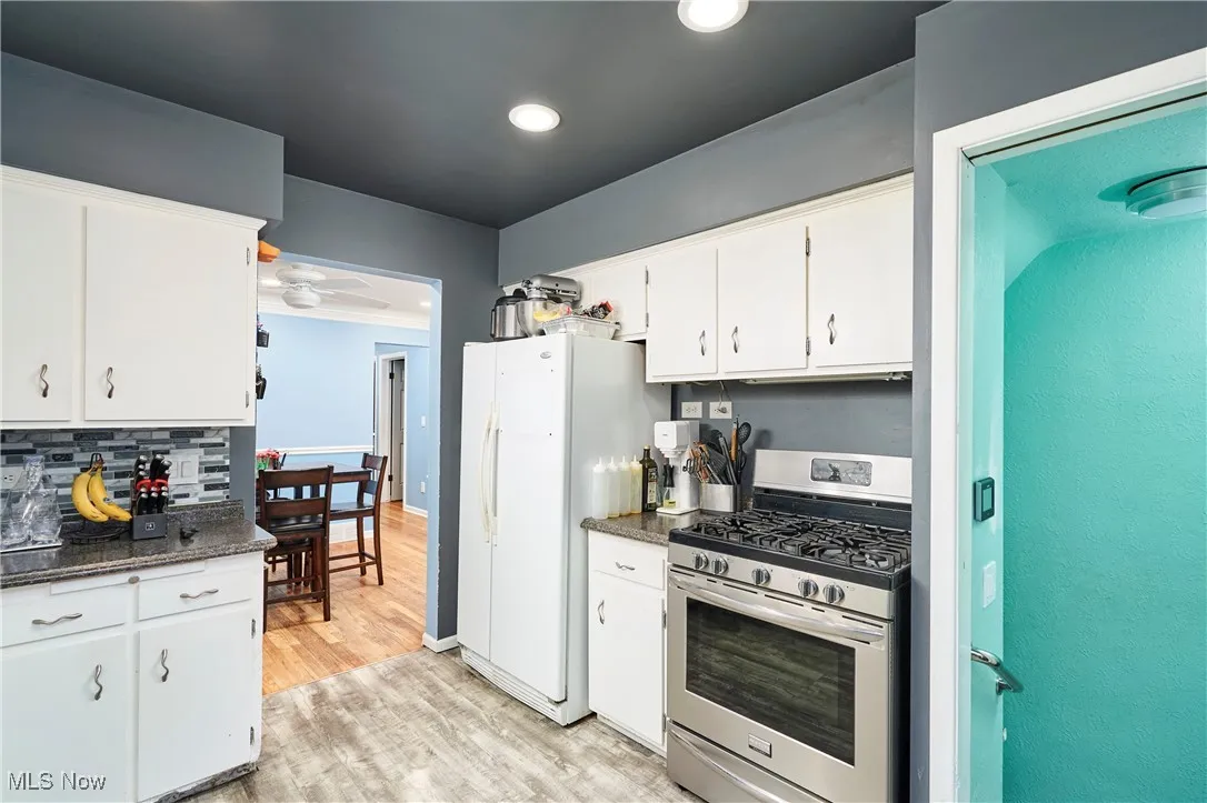 Kitchen with gas stove, white cabinetry, light wood finished floors, tasteful backsplash, and dark stone countertops