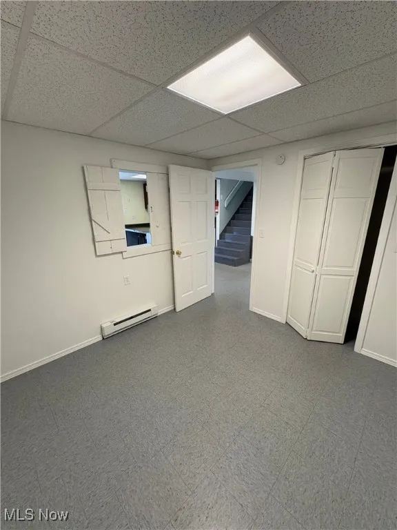 Finished basement with a paneled ceiling, tile patterned floors, a baseboard radiator, and stairs