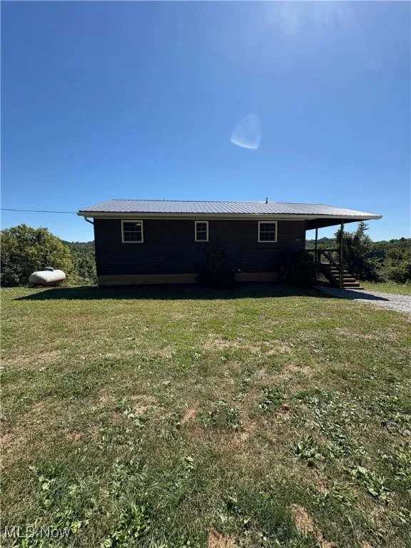 View of side of home featuring a metal roof, a lawn, and a porch