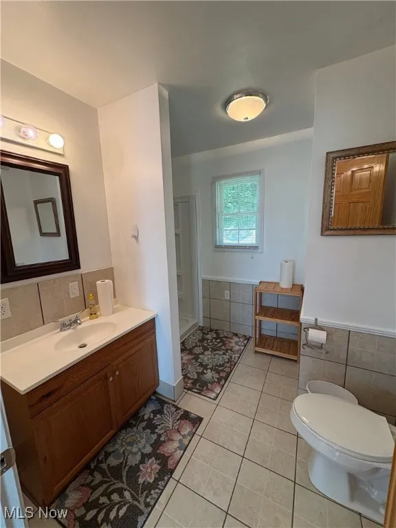 Full bath with light tile patterned flooring, vanity, tile walls, and a wainscoted wall