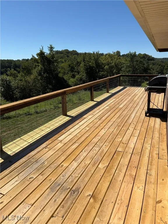 Wooden terrace featuring a wooded view and a grill