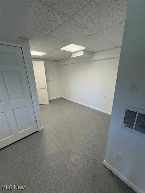 Empty room with tile patterned floors, a drop ceiling, and heating unit