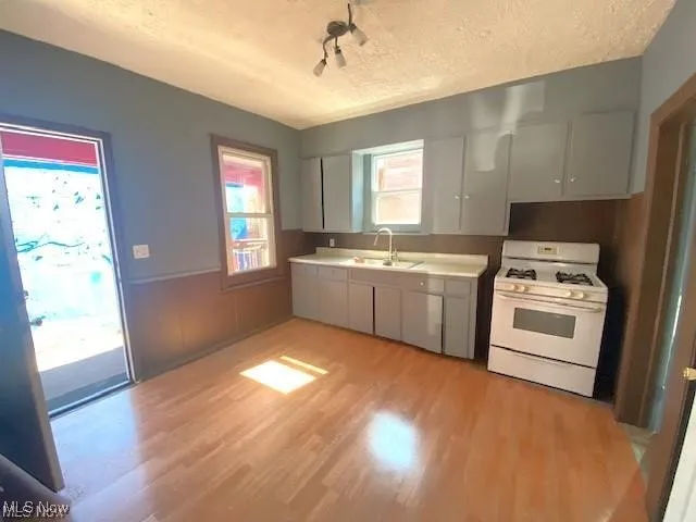 Kitchen featuring white range with gas cooktop, a textured ceiling, light wood-style floors, light countertops, and gray cabinetry