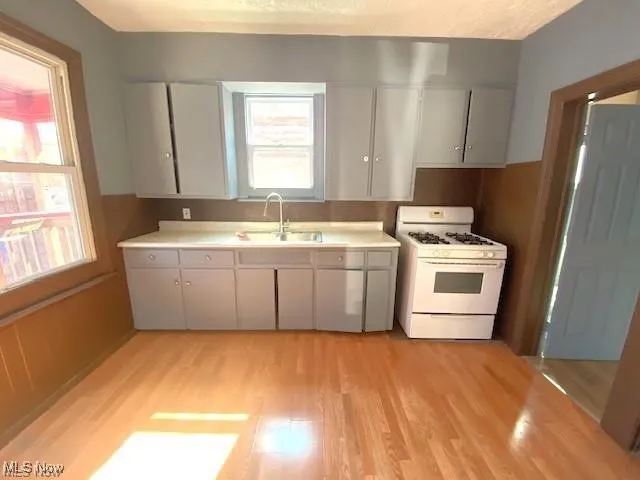 Kitchen with white gas stove, light countertops, light wood-type flooring, a textured ceiling, and gray cabinetry