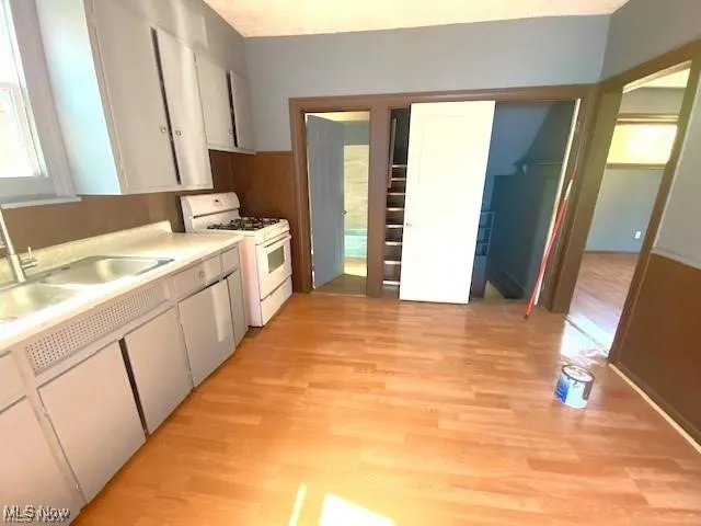 Kitchen with white gas stove, light wood finished floors, light countertops, and white cabinets