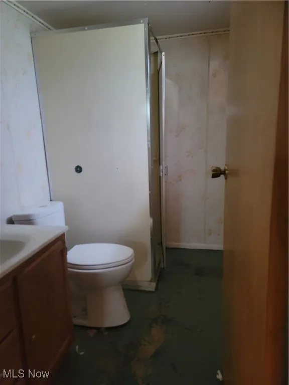 Full bathroom featuring wallpapered walls, vanity, a stall shower, and concrete floors