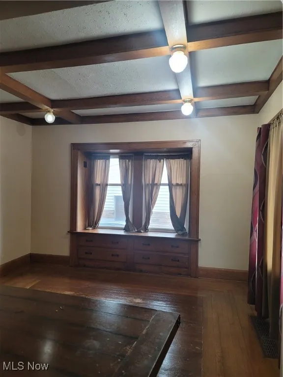 Spare room featuring beam ceiling, coffered ceiling, and dark wood finished floors