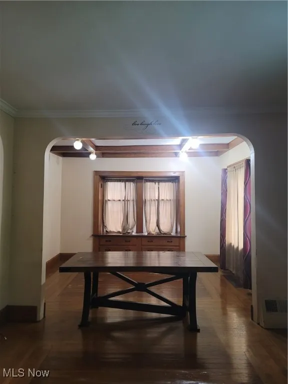 Dining area featuring arched walkways, dark wood-type flooring, and ornamental molding