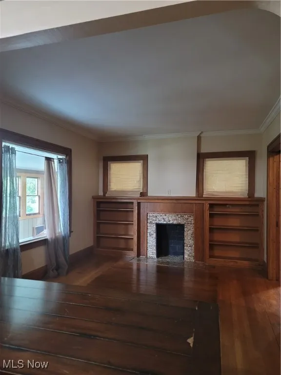 Unfurnished living room with ornamental molding, a tiled fireplace, and dark wood finished floors