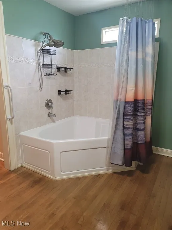 Full bath with wood finished floors and shower / bath combination with curtain