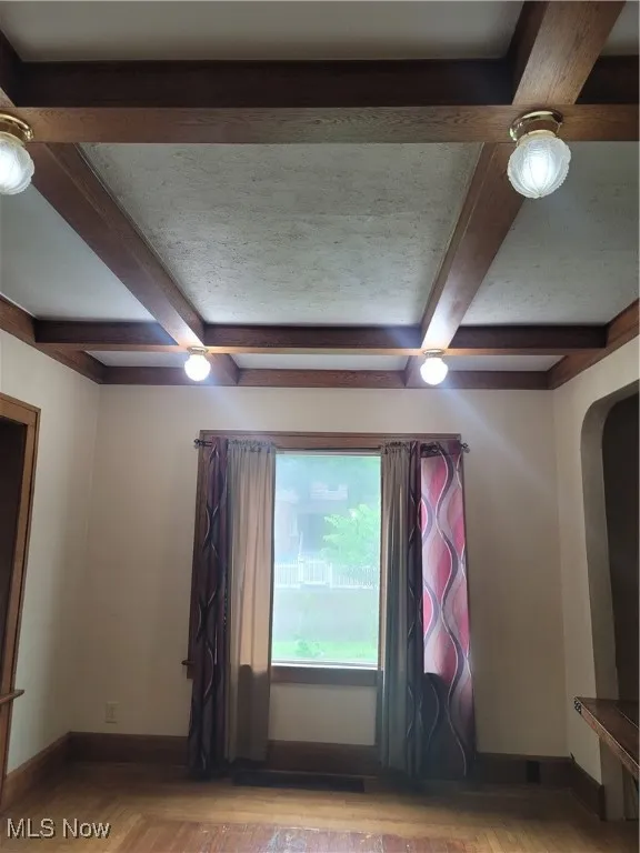 Empty room with beamed ceiling, arched walkways, wood finished floors, and coffered ceiling
