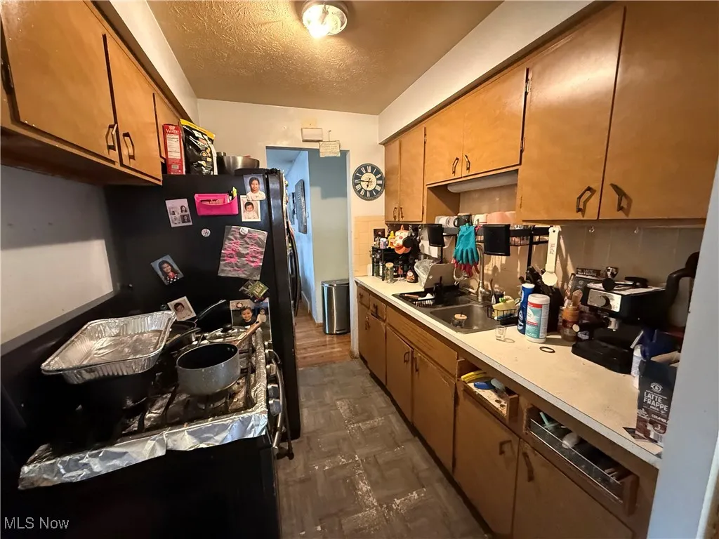 Kitchen with a textured ceiling, freestanding refrigerator, brown cabinets, and light countertops