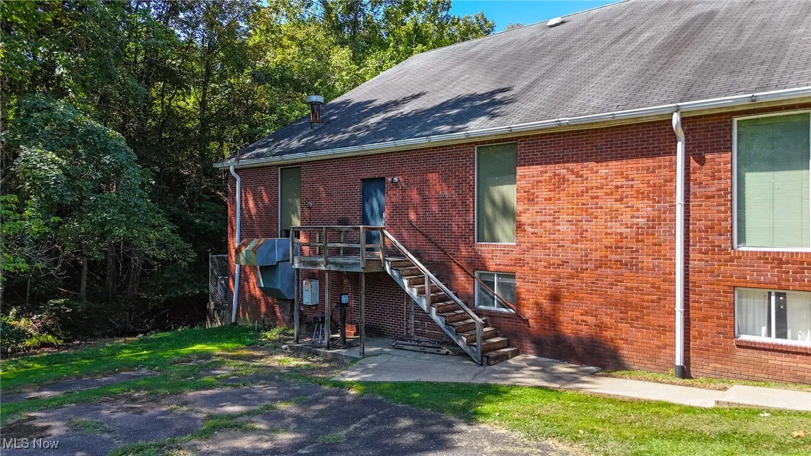 View of front of property with brick siding, stairs, and a shingled roof