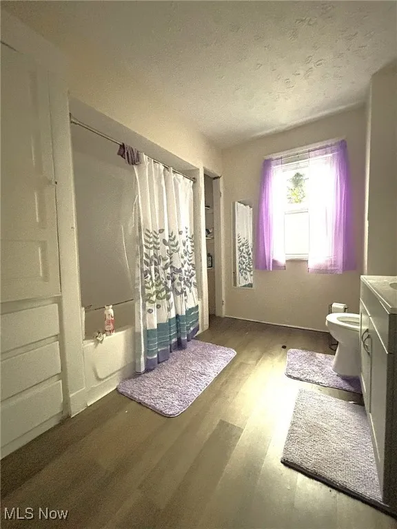 Bathroom featuring wood finished floors, shower / bath combo, vanity, and a textured ceiling