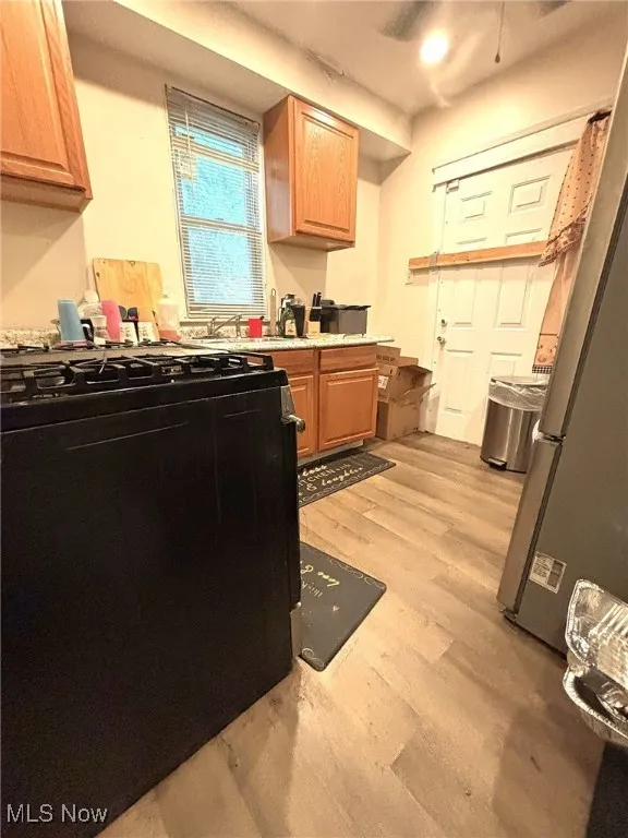 Kitchen with gas stove, light wood-type flooring, freestanding refrigerator, and brown cabinets