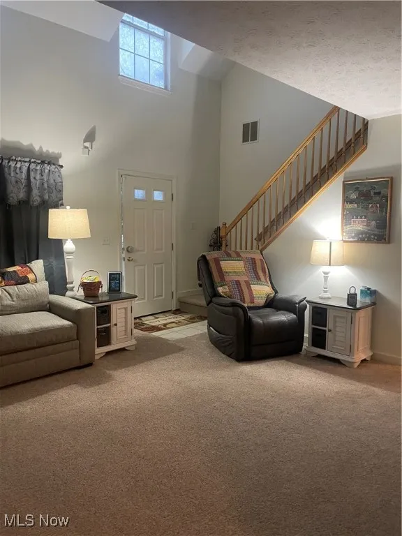 Living area featuring light colored carpet, stairs, and high vaulted ceiling