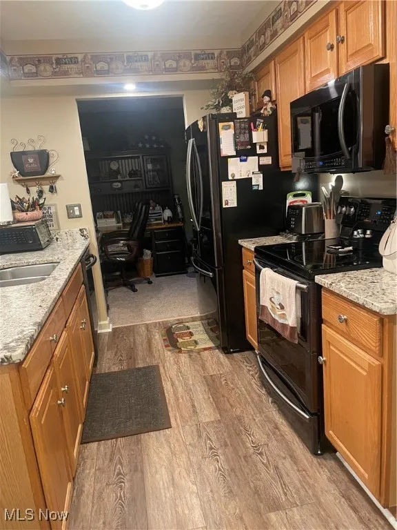 Kitchen featuring black appliances, light stone counters, brown cabinets, and light wood finished floors
